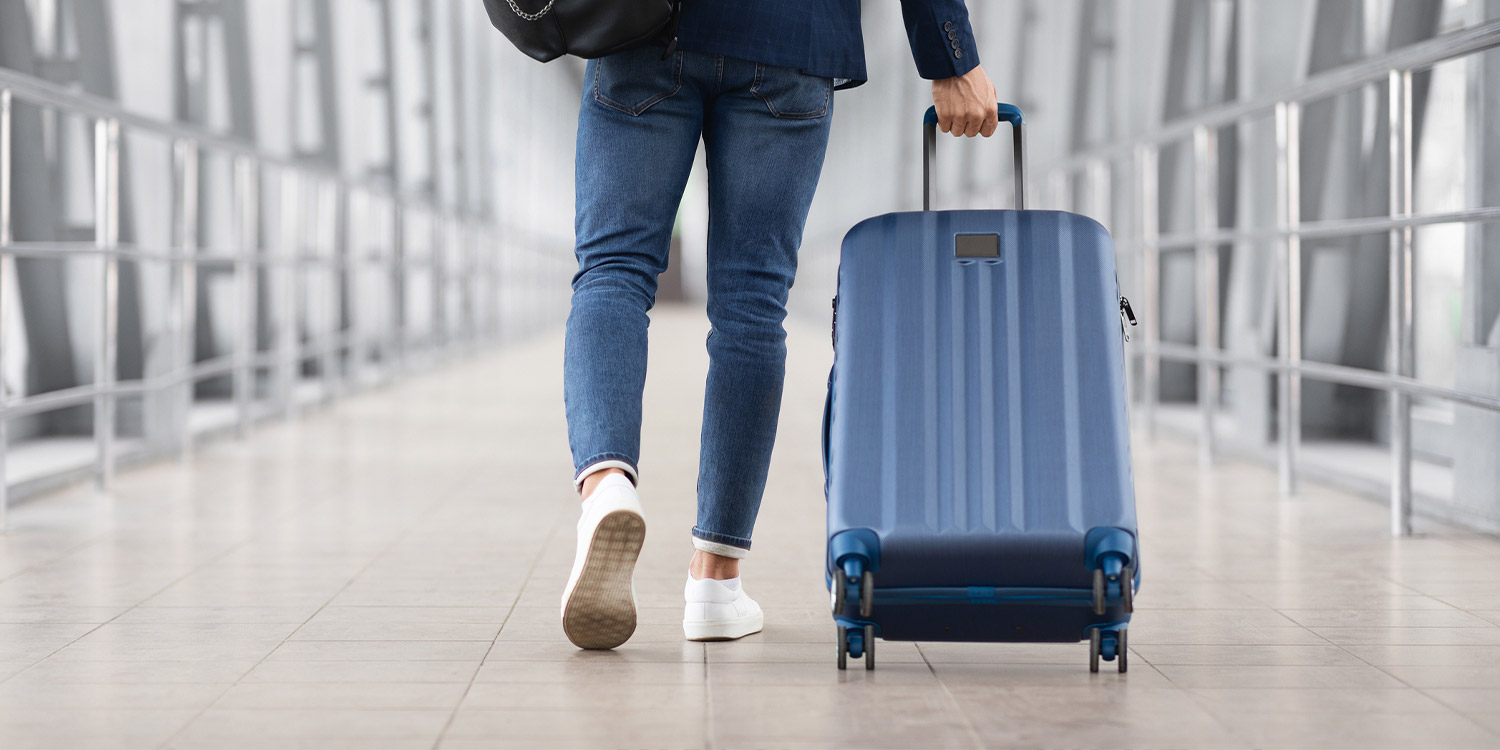 Man walks down a flight corridor with a wheeled suitcase.